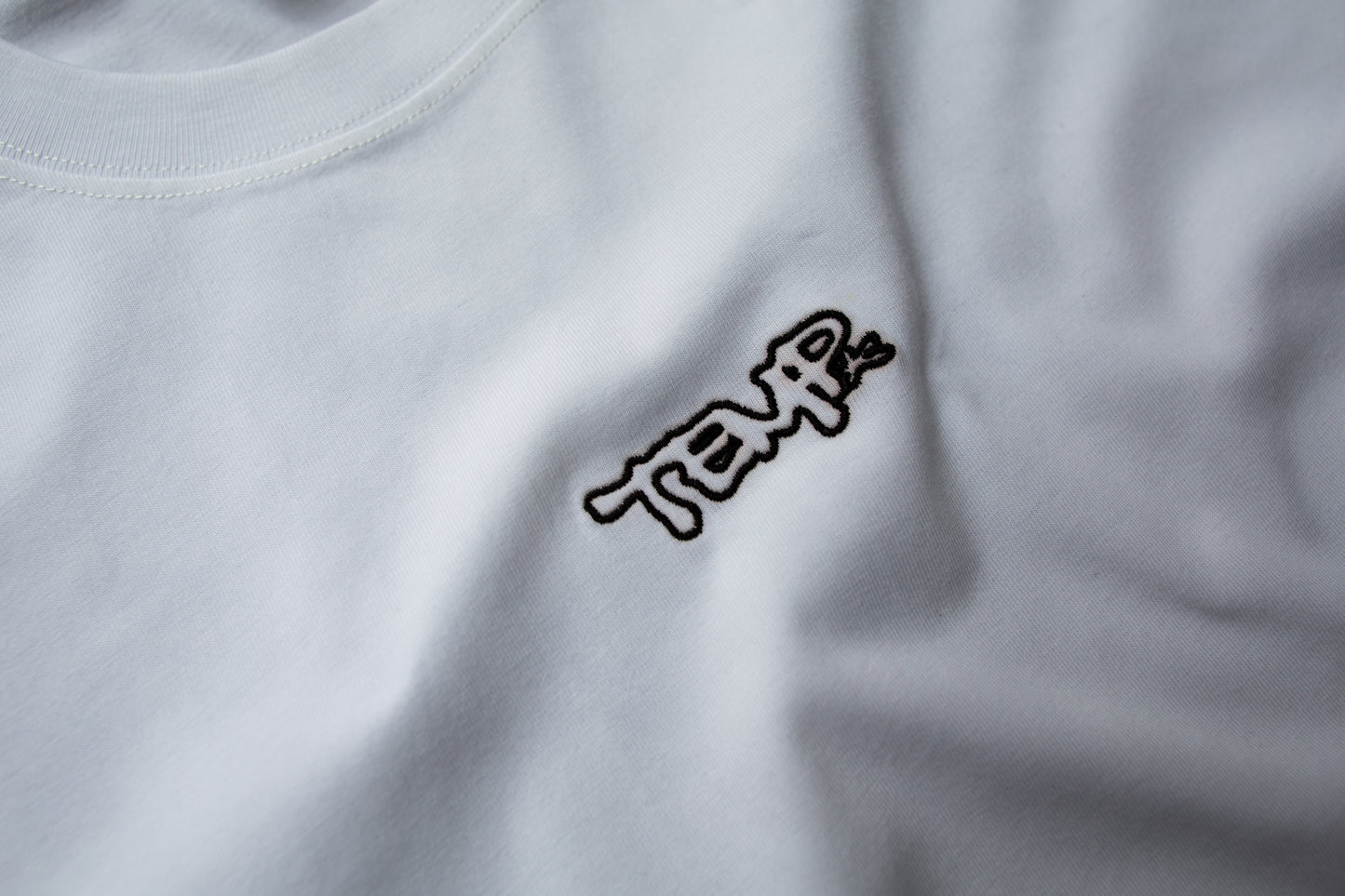 Close-up of a white shirt with a black logo on a plain background