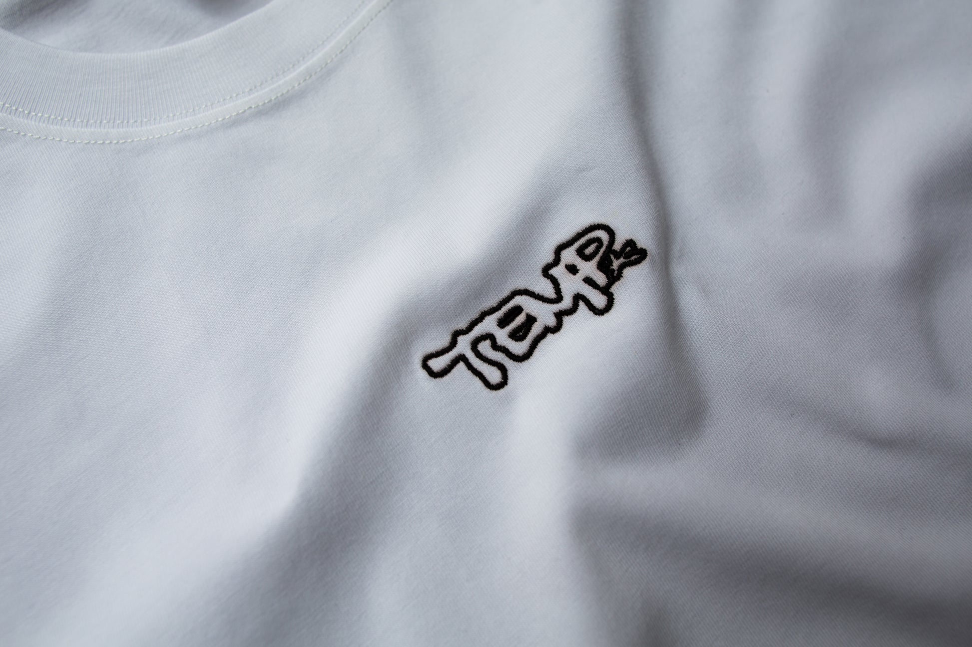 Close-up of a white shirt with a black logo on a plain background
